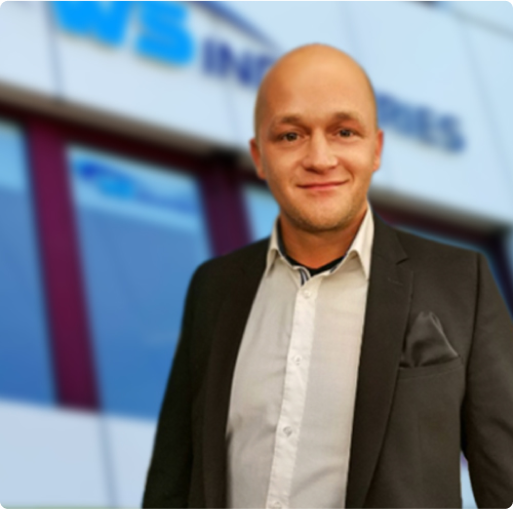 Mann in Anzug vor unscharfem Hintergrund mit Firmenlogo.