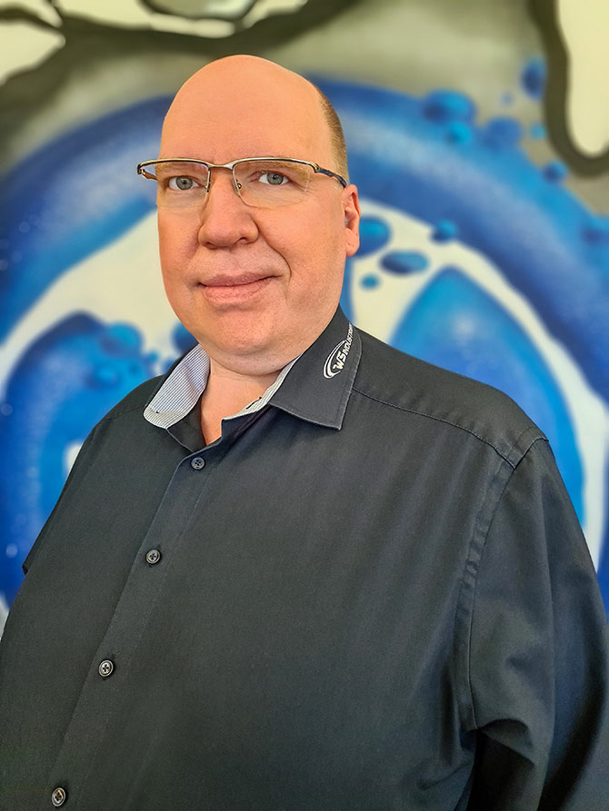 Mann mittleren Alters mit Brille vor Wandbild